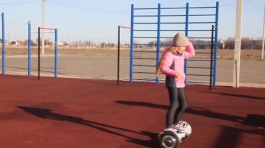 Kızıl saçlı kız kendini dengeleyen bir scooter 'a biniyor. Çocuk parkındaki çocuklar