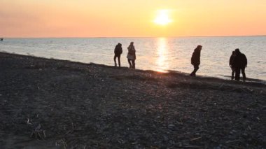 Çocuklar batan güneşin altında plajda koşar. Çocukların siluetleri