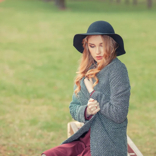 Chica en sombrero negro sentado en el parque — Foto de Stock