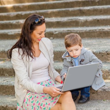 Anne ile oğlu ve parkta merdiven üstünde laptop