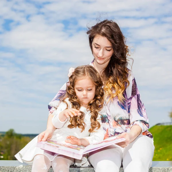 Mamma med dotter läsa en bok i parken — Stockfoto