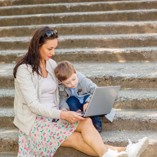 Mom with son and laptop on the stairs in the park