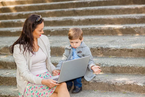 Mom with son and laptop on the stairs in the park — Stock Photo, Image