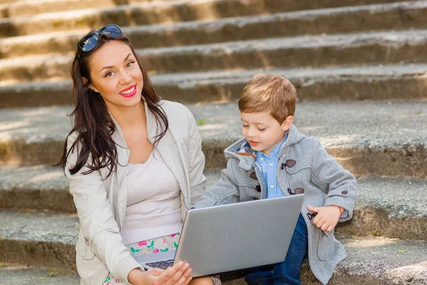 Mom with son and laptop on the stairs in the park