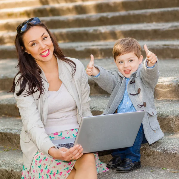 Mamma med son och laptop på trappan i parken Stockbild