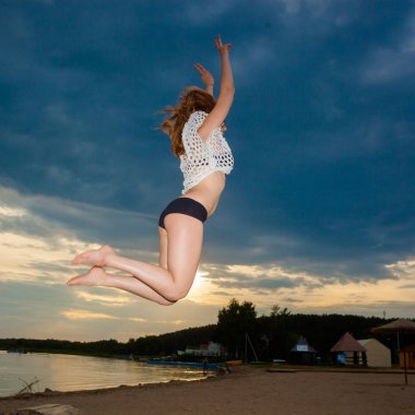 Kız sahilde günbatımı arka plan üzerinde atlama.