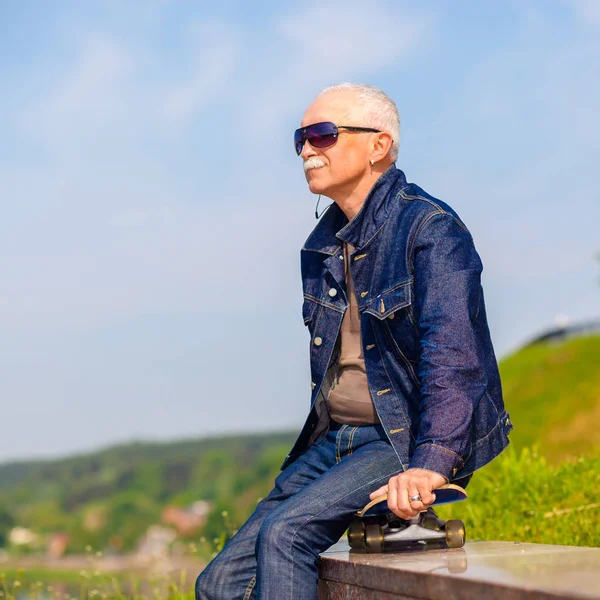 Senior man sitting and dreaming on the pavement near a skateboard — Stock Photo, Image