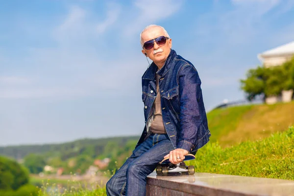 Senior man zitten en dromen op de stoep in de buurt van een skateboard — Stockfoto