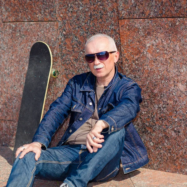 Senior man sitting and dreaming on the pavement near a skateboard — Stock Photo, Image