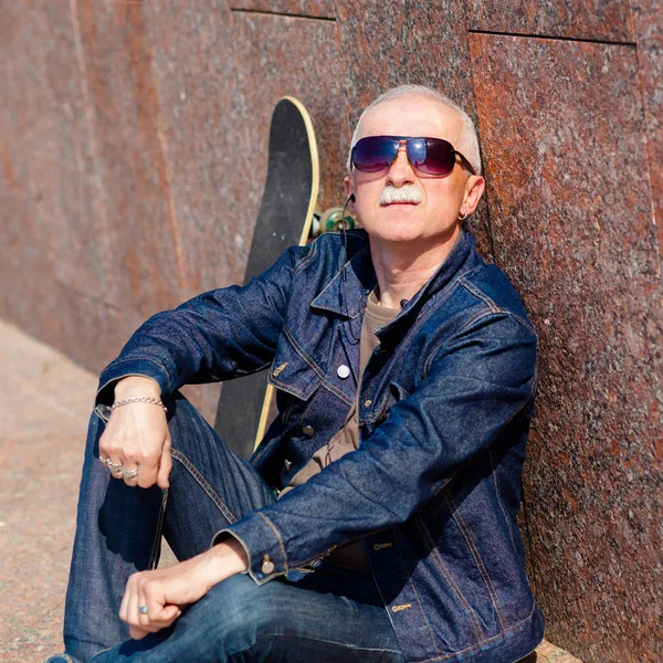 Senior man sitting and dreaming on the pavement near a skateboard — Stock Photo, Image