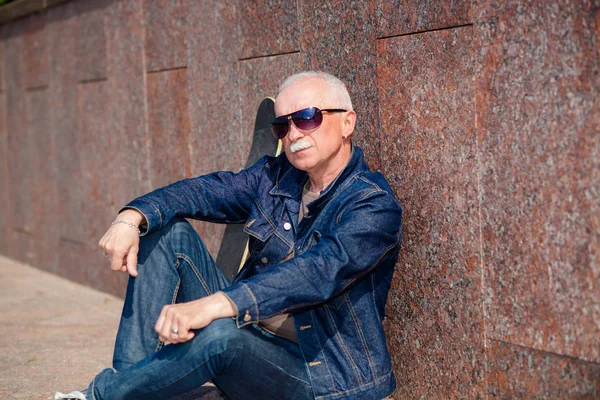 Senior man sitting and dreaming on the pavement near a skateboard — Stock Photo, Image