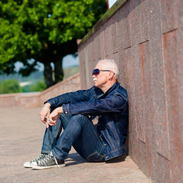 Äldre man sitter och drömmer på trottoaren nära en skateboard — Stockfoto