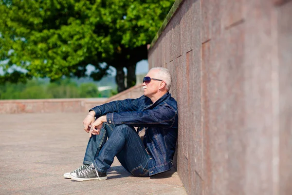 Senior man sitting and dreaming on the pavement near a skateboard — Stock Photo, Image