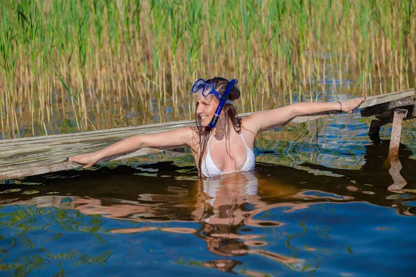 Happy diving girl in a swimming mask and snorkel near the old wooden pier. — Stock Photo, Image