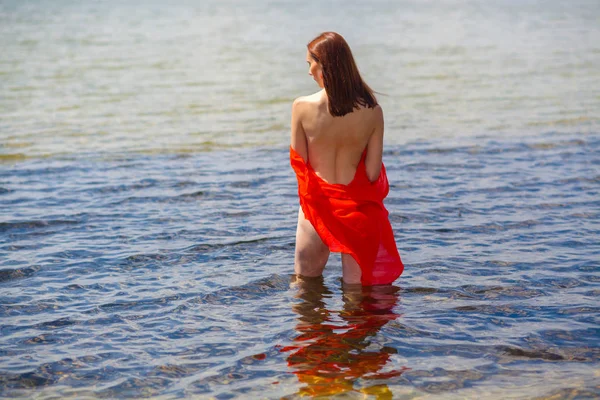 Fille avec un dos nu dans une chemise rouge va dans l'eau . — Photo