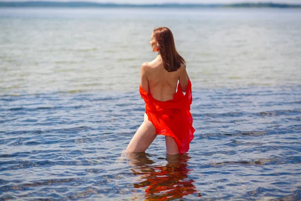 Mädchen mit nacktem Rücken im roten Hemd geht ins Wasser. — Stockfoto