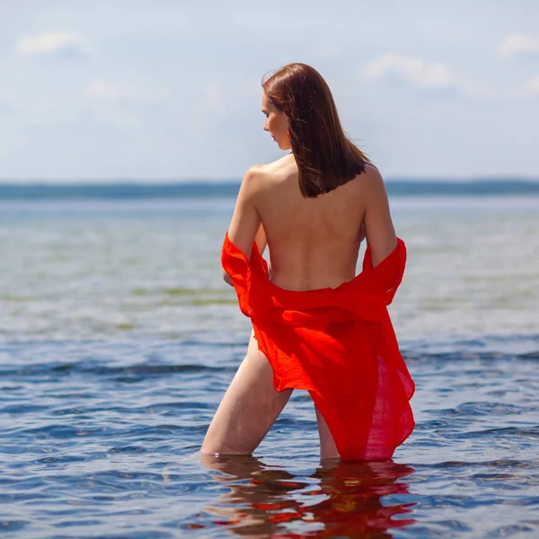 Girl with a naked back in a red shirt goes into the water.