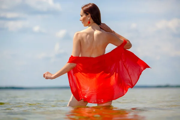 Mädchen mit nacktem Rücken im roten Hemd geht ins Wasser. — Stockfoto