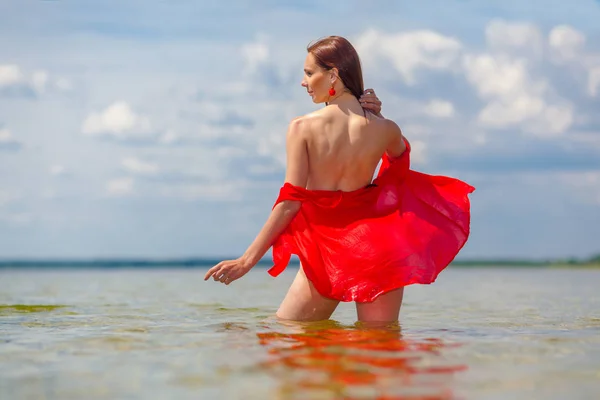 Ragazza con una schiena nuda in camicia rossa va in acqua . — Foto Stock