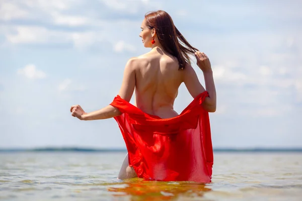 Dívka s nahou zpět v červené košili jde do vody. — Stock fotografie