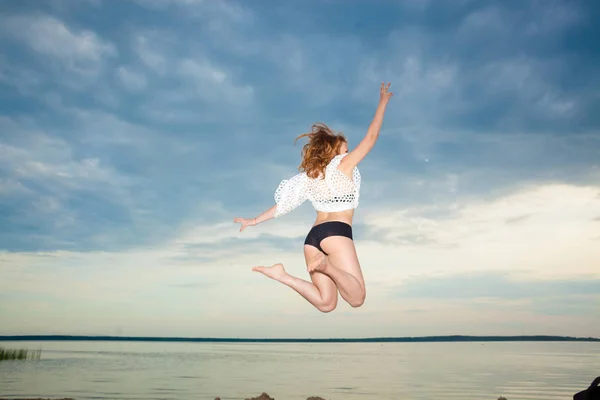 Kız sahilde günbatımı arka plan üzerinde atlama. — Stok fotoğraf
