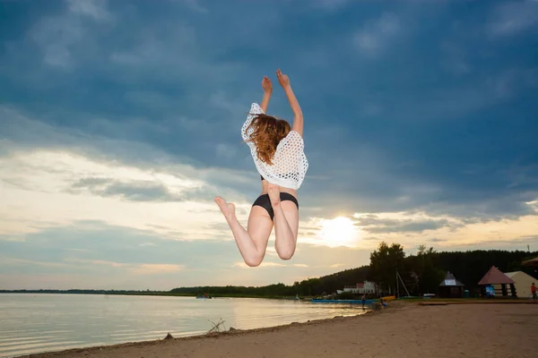 Dívka, která skočila na pláži při západu slunce pozadí. — Stock fotografie