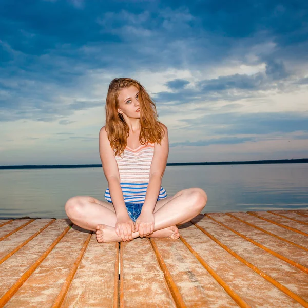Dziewczyna na molo na plaży medytuje na zachód słońca. — Zdjęcie stockowe
