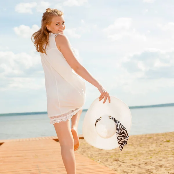 Романтична дівчина в білій сукні з білим капелюхом звернулася до довгохвостого дерев'яного пірсу на пляжі . — стокове фото