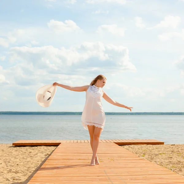 Romantic girl in a white dress with a white hat turned to the long-tailed wooden pier on the beach. — Stock Photo, Image