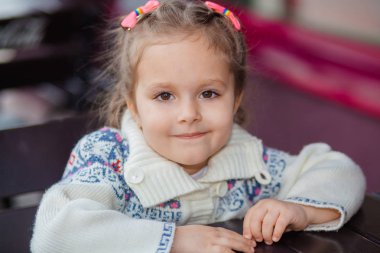 Duygusal kız bir kafede bir masada. Yaz gününde açık restoranda oturan sevimli küçük kız. çocuk onun emri için bekleyen bir kafede. 