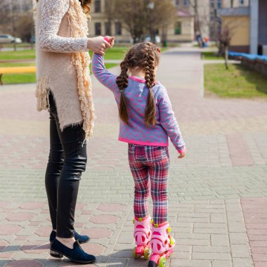 Anne ve kızı tekerlekli paten üzerinde binmek. Kız paten ve falls öğrenme. Anne kızı Silindirler binmek için öğretir