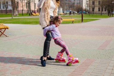 Anne ve kızı tekerlekli paten üzerinde binmek. Kız paten ve falls öğrenme. Anne kızı Silindirler binmek için öğretir