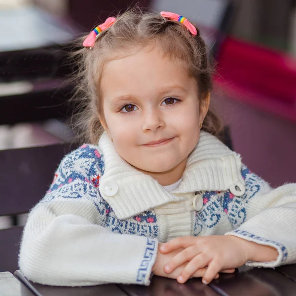 Эмоциональная девушка за столом в кафе. Милая маленькая девочка сидит в ресторане на открытом воздухе в летний день. ребенок в кафе ждет своего заказа . — стоковое фото