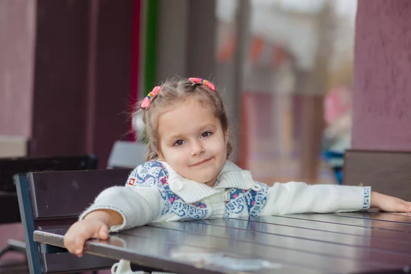 Ragazza emotiva a un tavolo in un bar. Ragazzina carina seduta nel ristorante all'aperto il giorno d'estate. bambino in un caffè in attesa del suo ordine . — Foto Stock