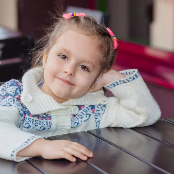 Menina emocional em uma mesa em um café. Menina bonito sentado no restaurante ao ar livre no dia de verão. criança em um café à espera de sua ordem . — Fotografia de Stock