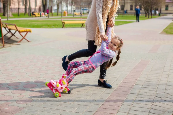 Mama i córka jeździć na rolkach. Dziewczyna uczenia się do rolki i upadki. Mama uczy córkę do jazdy na rolkach — Zdjęcie stockowe