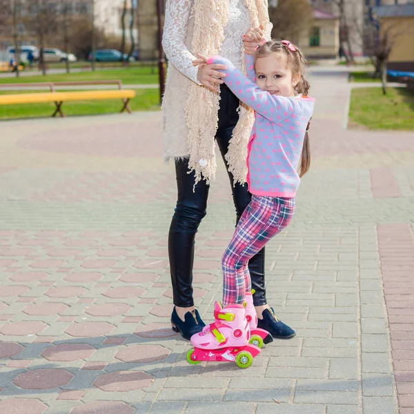 Mamma och dotter rida på rullskridskor. Flicka lära sig roller skate och falls. Mamma lär dotter att rida på rullarna — Stockfoto