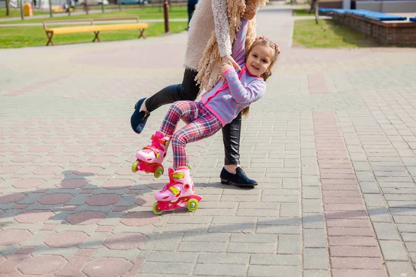 Mamma och dotter rida på rullskridskor. Flicka lära sig roller skate och falls. Mamma lär dotter att rida på rullarna — Stockfoto