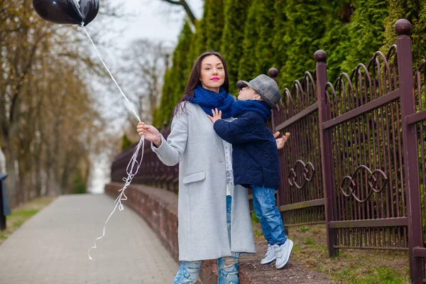 Porträt des modischen Jungen und seiner wunderschönen Mutter inmitten von Luftballons. Kleiner Junge umarmt seine Mutter emotional. — Stockfoto