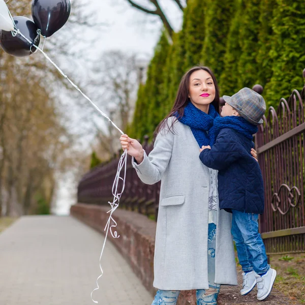 Porträtt av fashionabla pojke och hans underbara mor bland ballonger. liten pojke kramar sin mor känslomässigt. — Stockfoto
