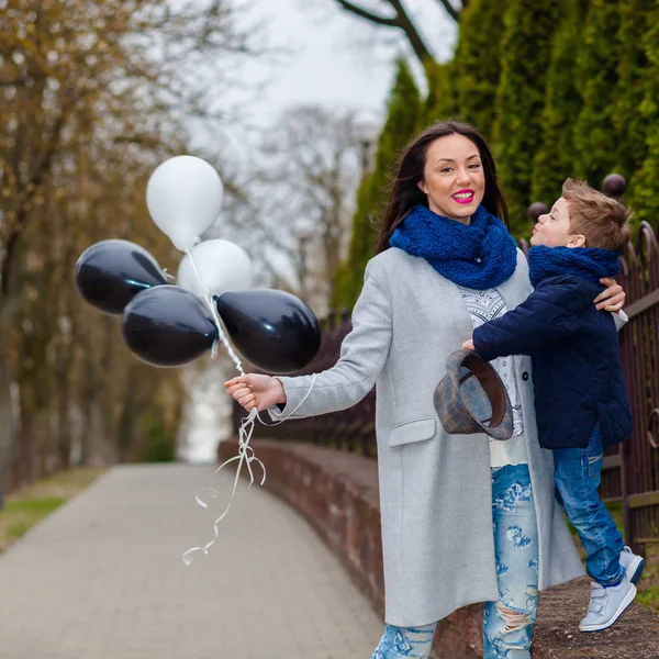 Porträtt av fashionabla pojke och hans underbara mor bland ballonger. liten pojke kramar sin mor känslomässigt. — Stockfoto