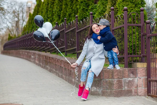Porträt des modischen Jungen und seiner wunderschönen Mutter inmitten von Luftballons. Kleiner Junge umarmt seine Mutter emotional. — Stockfoto