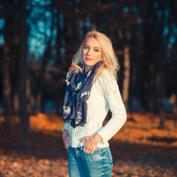 Schöne blonde Mädchen in einem weißen Pullover friert im Park — Stockfoto