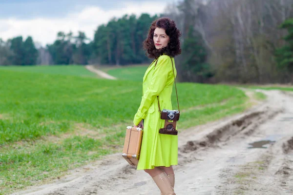 Hipster girl with a suitcase and a retro camera on the road — Stock Photo, Image