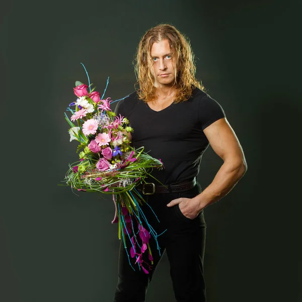 Homem musculoso viril com cabelos longos segura nas mãos um buquê de design de flores — Fotografia de Stock