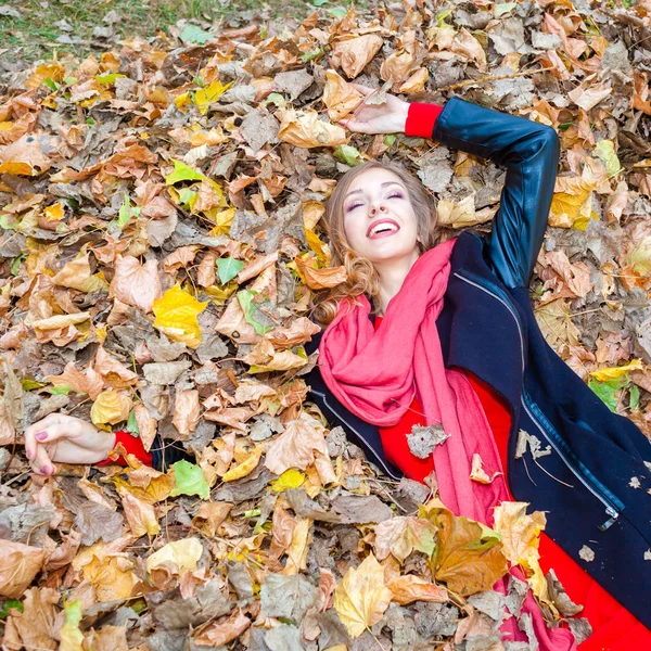 Cheerful positive dreamy girl lying among the leaves in the park — Stock Photo, Image