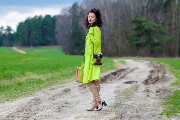 Hipster menina com uma mala e uma câmera retro na estrada — Fotografia de Stock