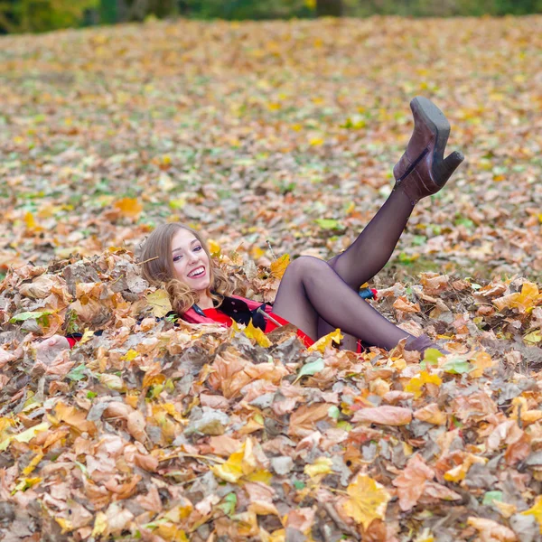 Cheerful positive dreamy girl lying among the leaves in the park — Stock Photo, Image