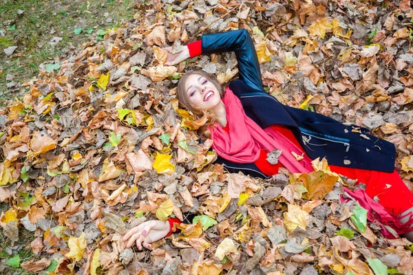 Glad positiv drömmande flicka liggande bland bladen i parken — Stockfoto