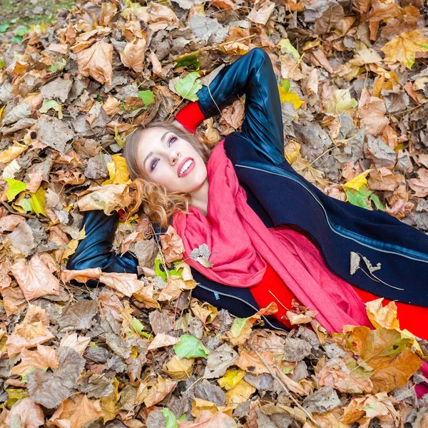 Cheerful positive dreamy girl lying among the leaves in the park — Stock Photo, Image